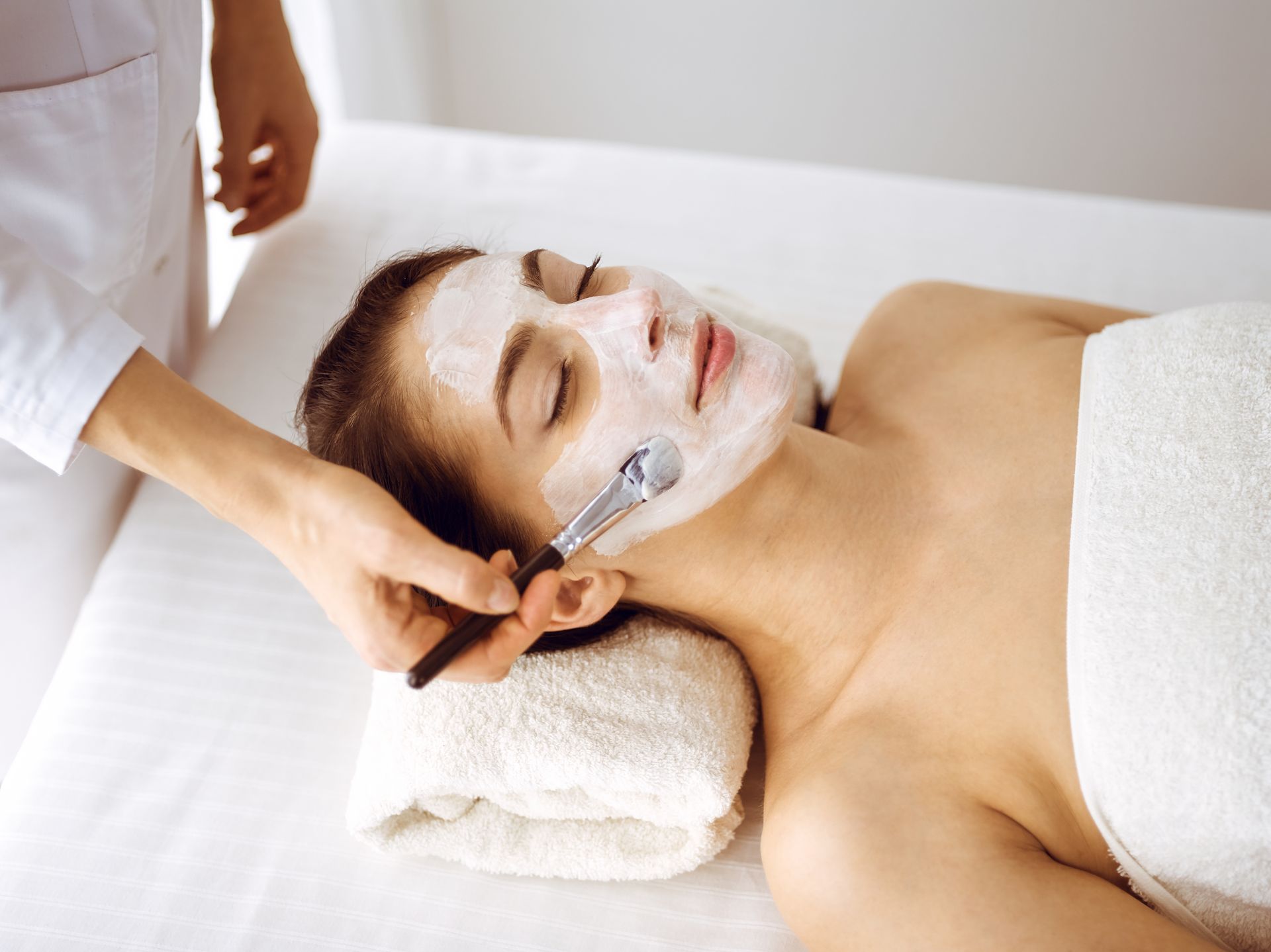 Spa facial treatment with a white mask being applied to a reclining client