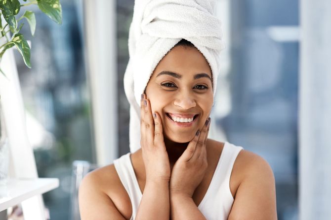 a woman with a towel wrapped around her head is smiling and touching her face .