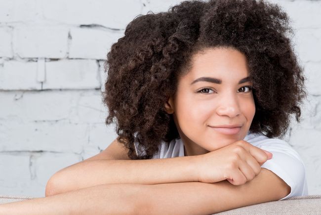 a young woman with curly hair is laying on a couch with her head resting on her arm .