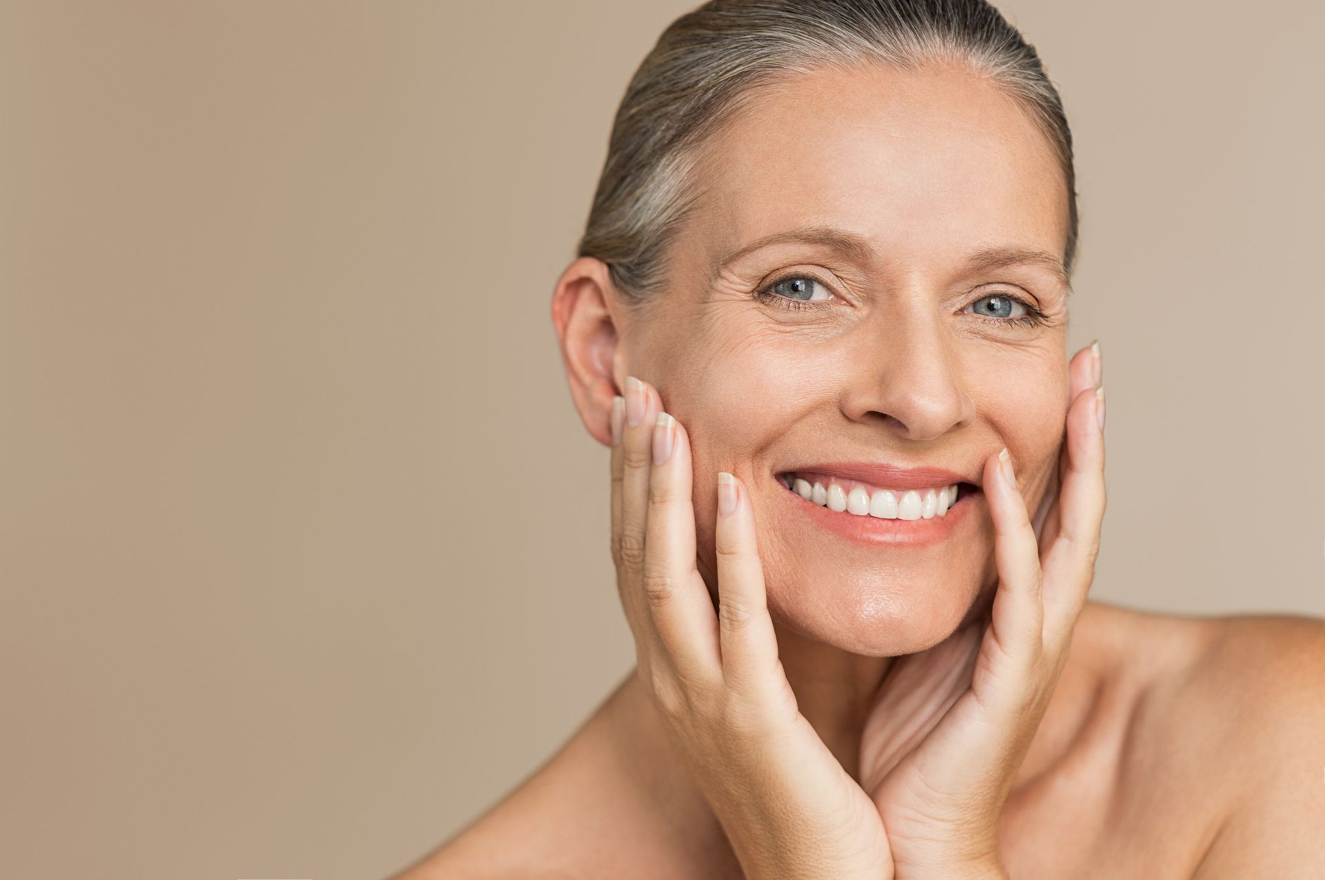 A woman is smiling and touching her face with her hands.