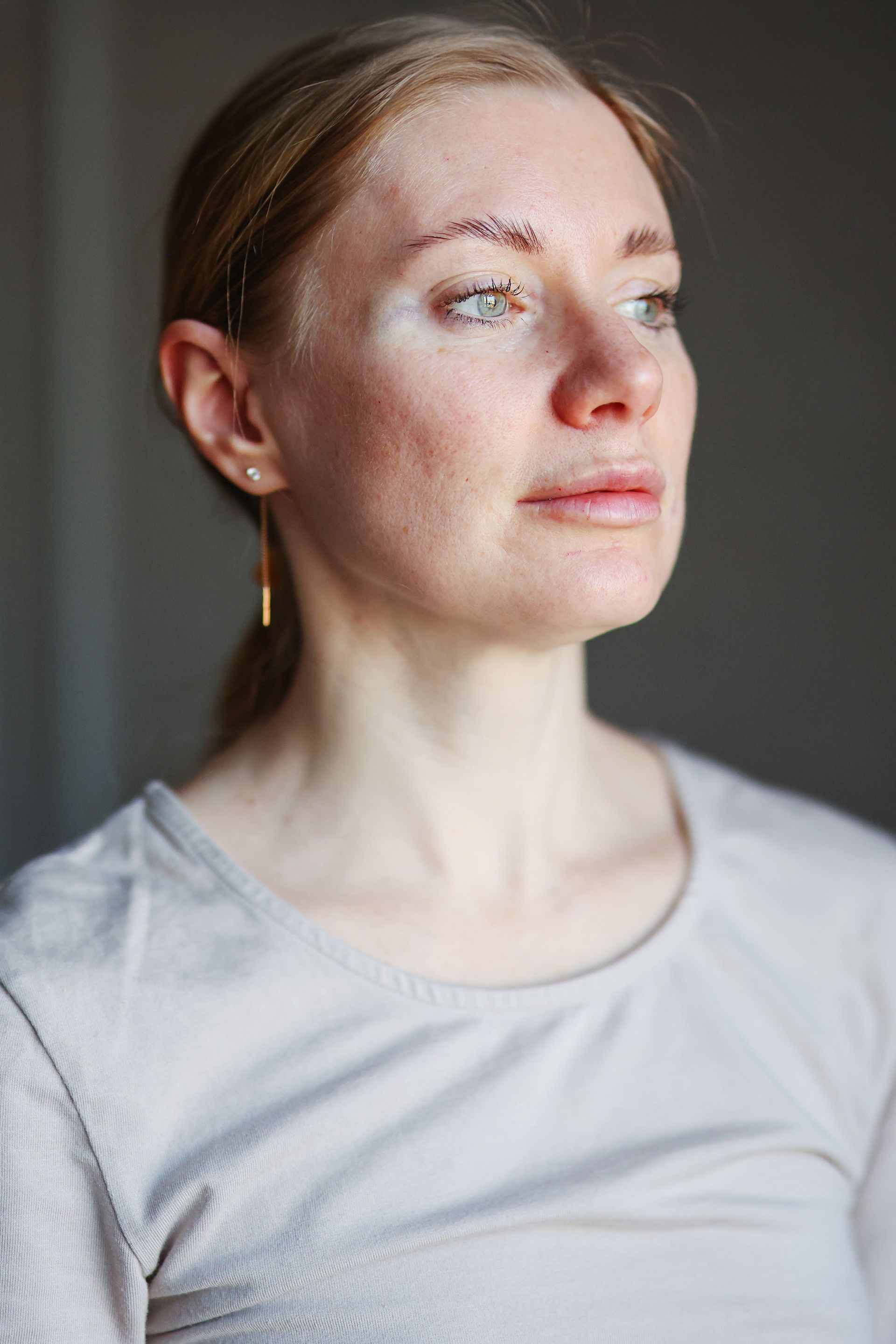 Woman with light skin, looking upwards, in neutral-colored sweater, with gold earrings.