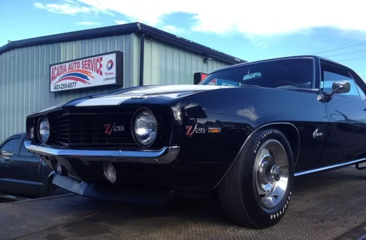 Black 1969 Chevrolet Camaro Z/28 with white racing stripes in front of an auto repair shop under a blue sky. | Acadia Auto Service