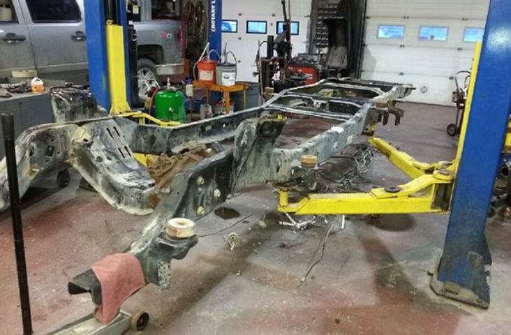 A vehicle frame on a lift in a garage; rust evident; tools and equipment around. | Acadia Auto Service