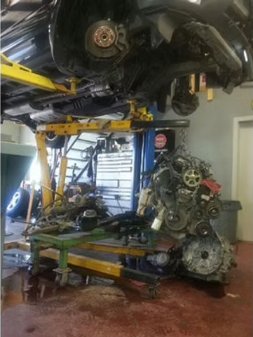 Car on a lift with the engine removed, sitting on a work bench in a garage. | Acadia Auto Service