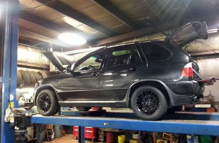 Black SUV raised on a lift in a garage with hood and trunk open, wheels are black. | Acadia Auto Service