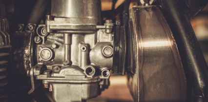Close-up of a motorcycle carburetor, showing metal components and bolts. | Acadia Auto Service
