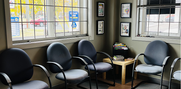 Waiting room with four chairs, small table, and framed pictures on the wall. A window shows the outdoors. | Acadia Auto Service