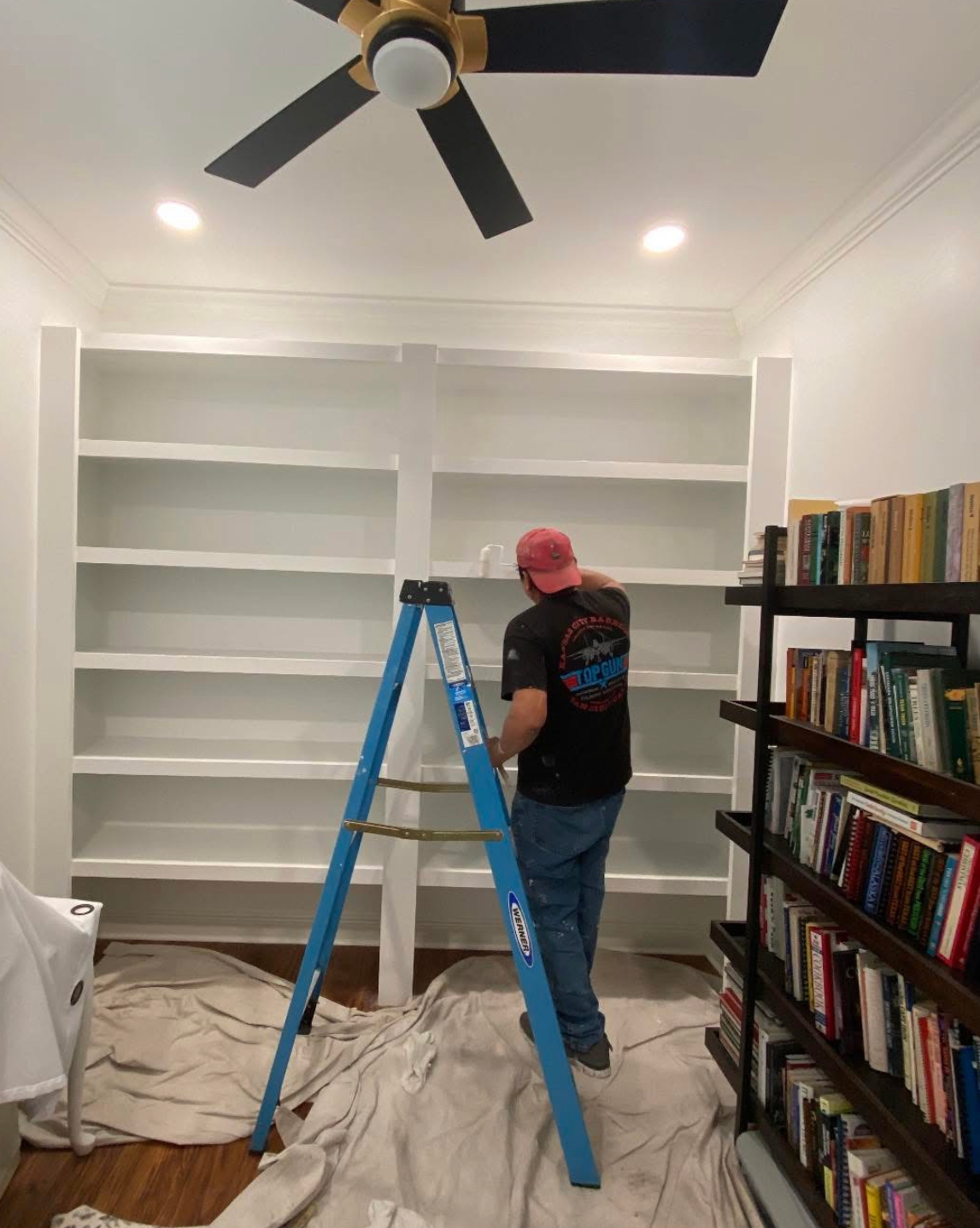 A man is standing on a ladder in front of a bookshelf.