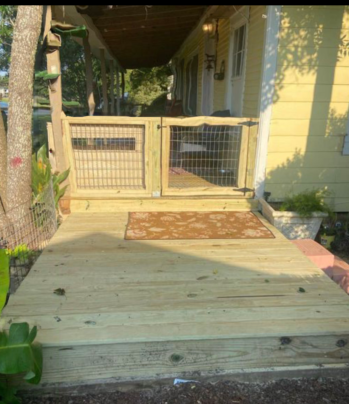 A wooden deck with a gate and stairs leading to a yellow house.