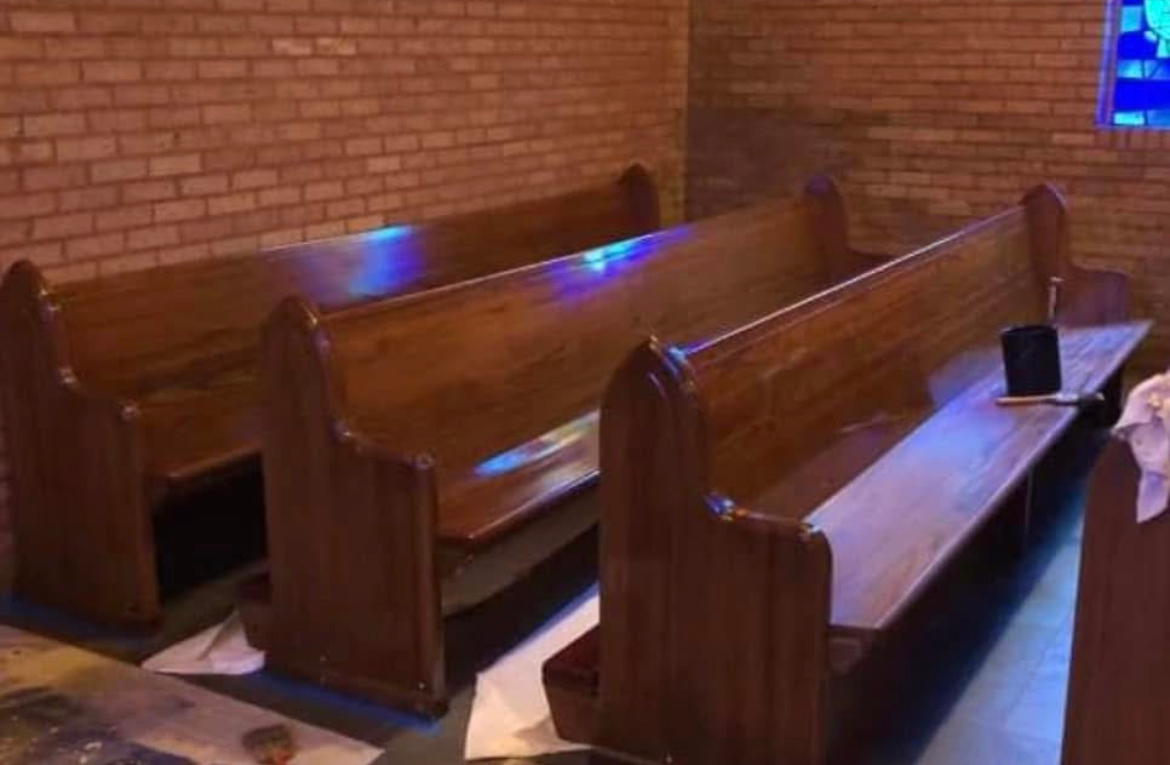 A row of wooden benches in a church with a brick wall.