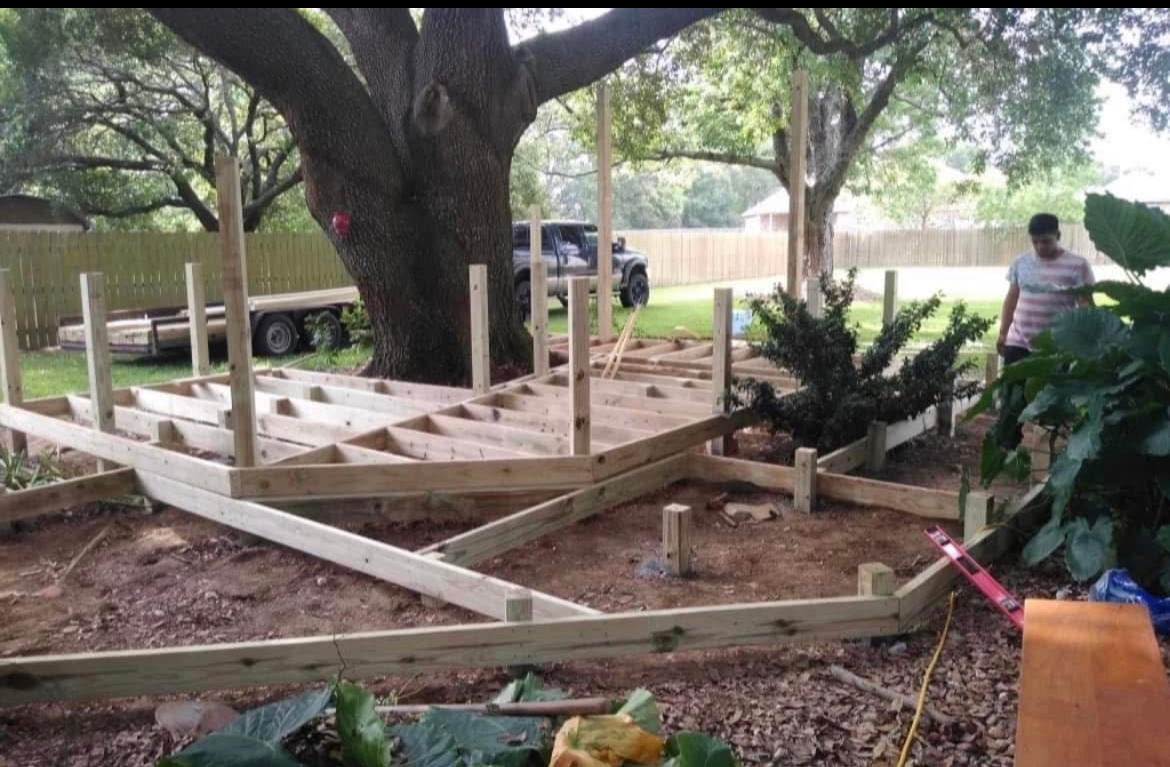 A wooden deck is being built in a backyard with a large tree in the background.