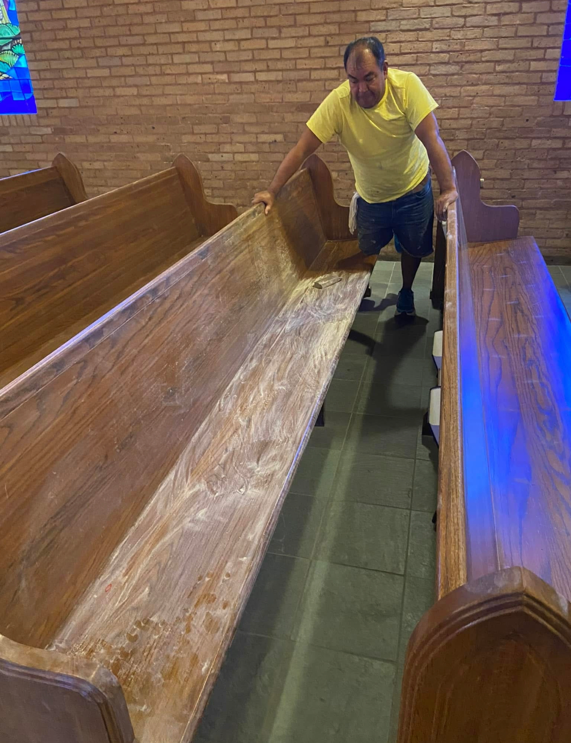 A man in a yellow shirt is standing next to a wooden bench in a church.