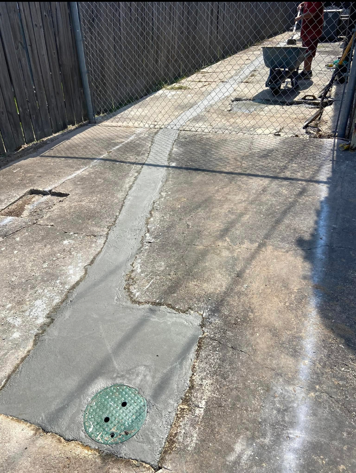 A man is working on a concrete driveway with a wheelbarrow.