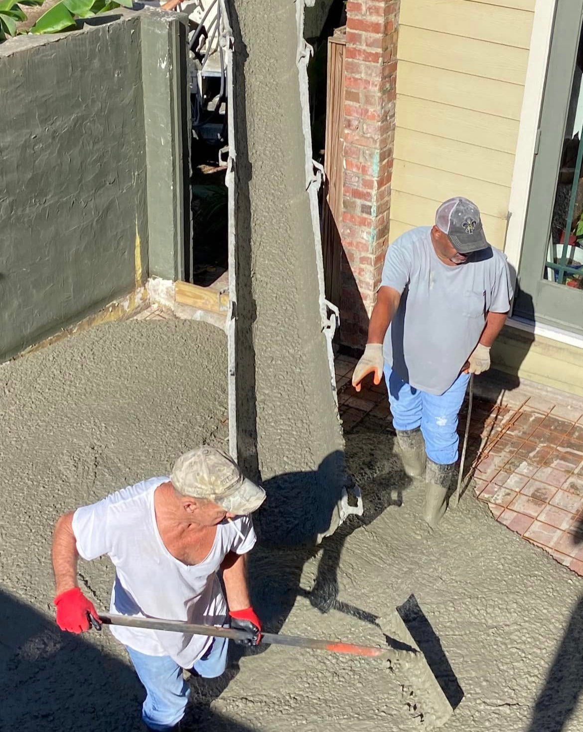 Two men are working on a concrete driveway in front of a house.