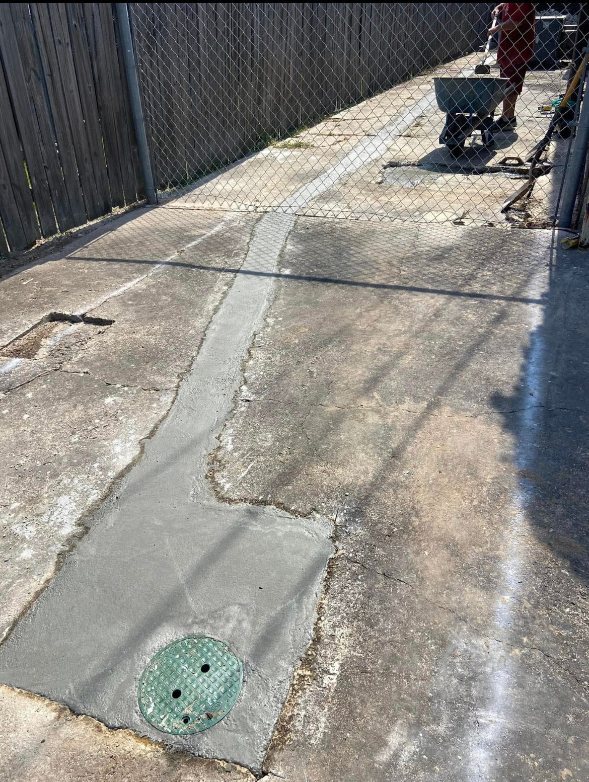 A man is working on a concrete driveway with a wheelbarrow.