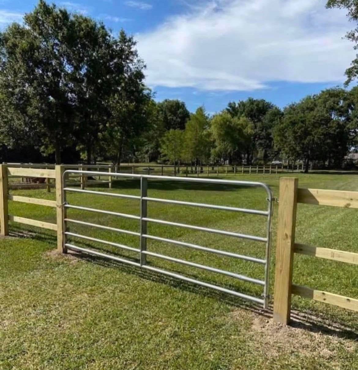 A wooden fence with a metal gate in the middle of a grassy field