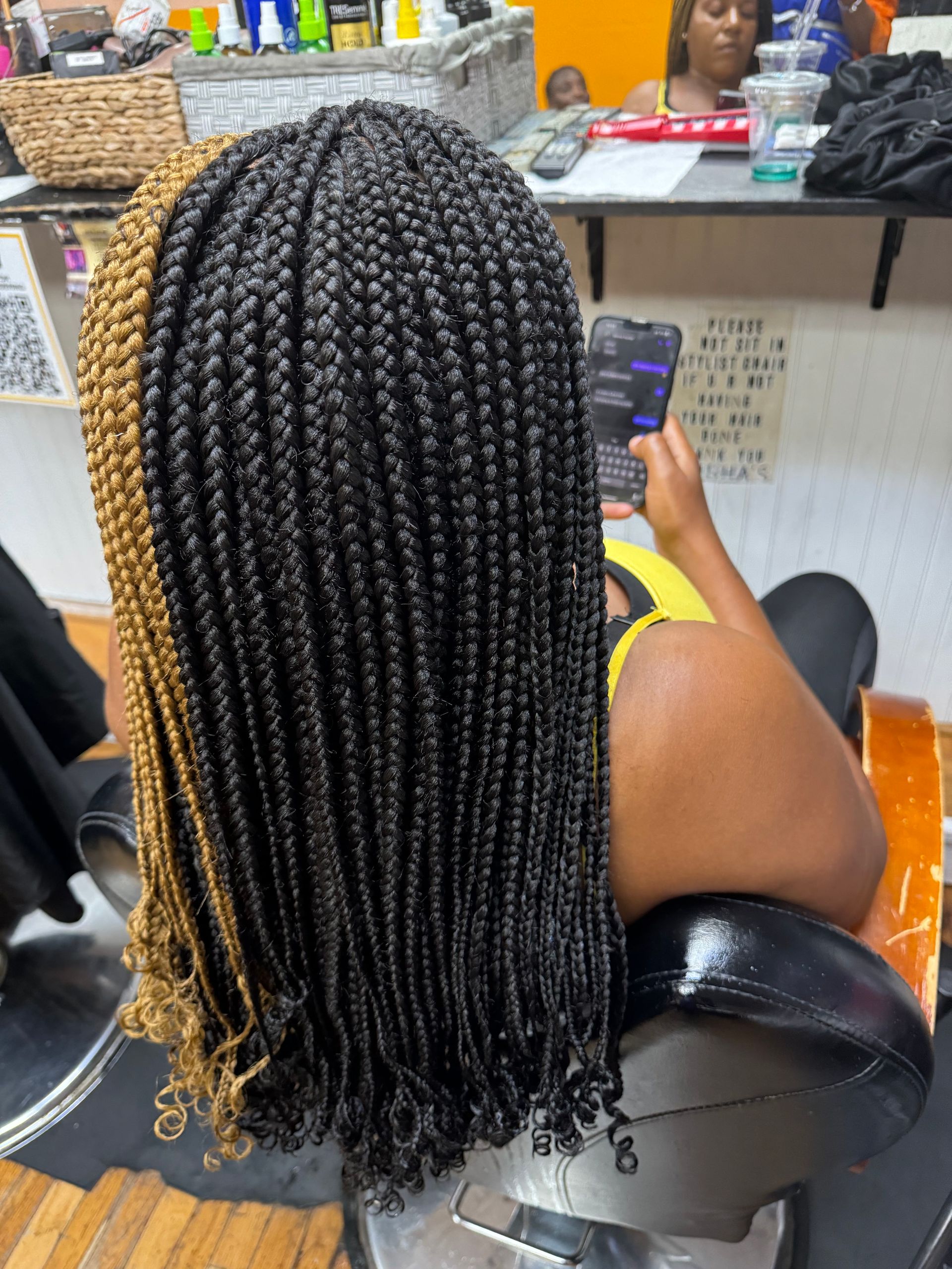 A woman with braids is sitting in a chair and looking at her phone. | Los Angeles, CA | Aissata & Al Diouma