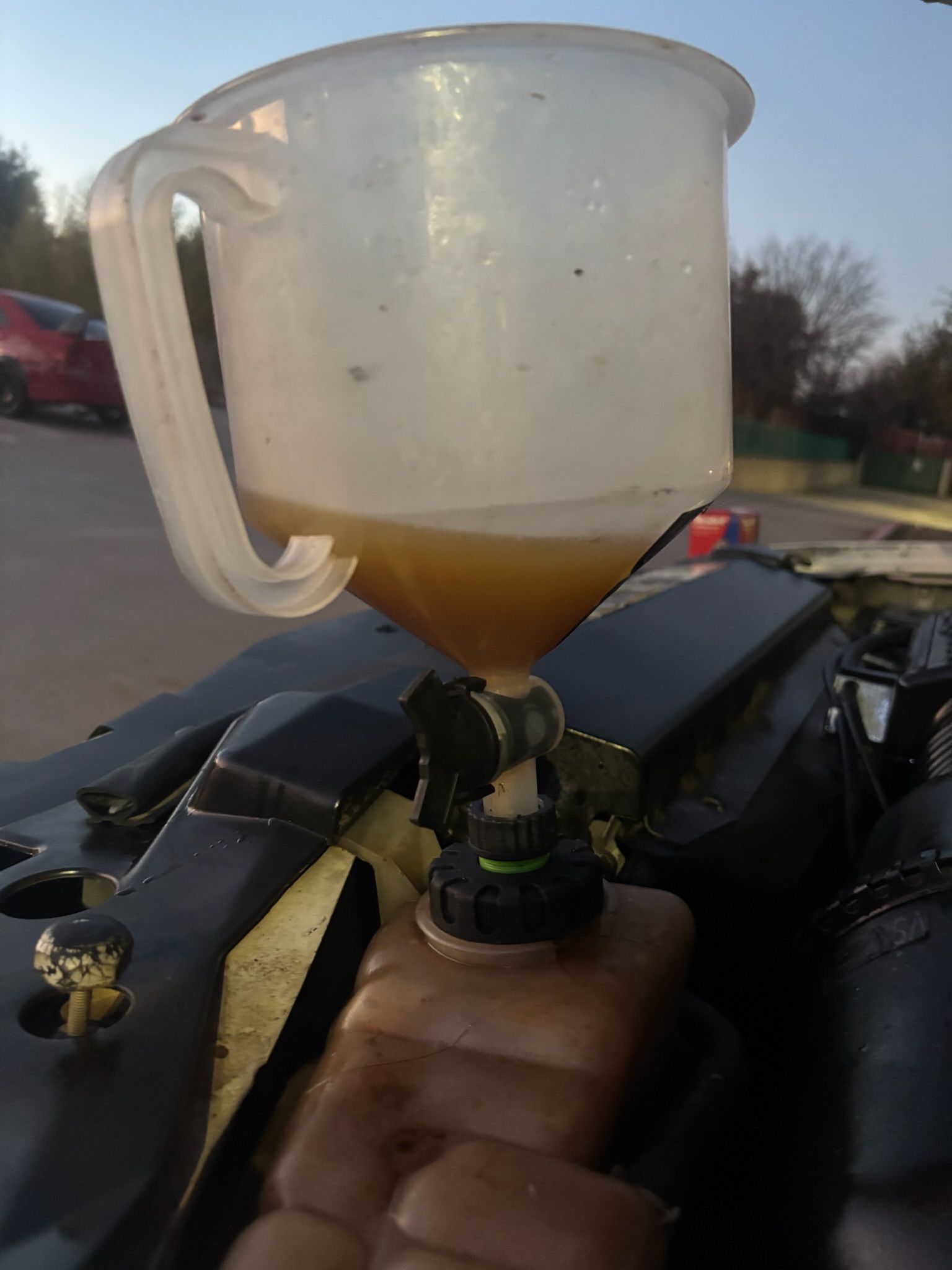Plastic cup mounted on a hand-held device, partly filled with amber liquid outdoors at sunset