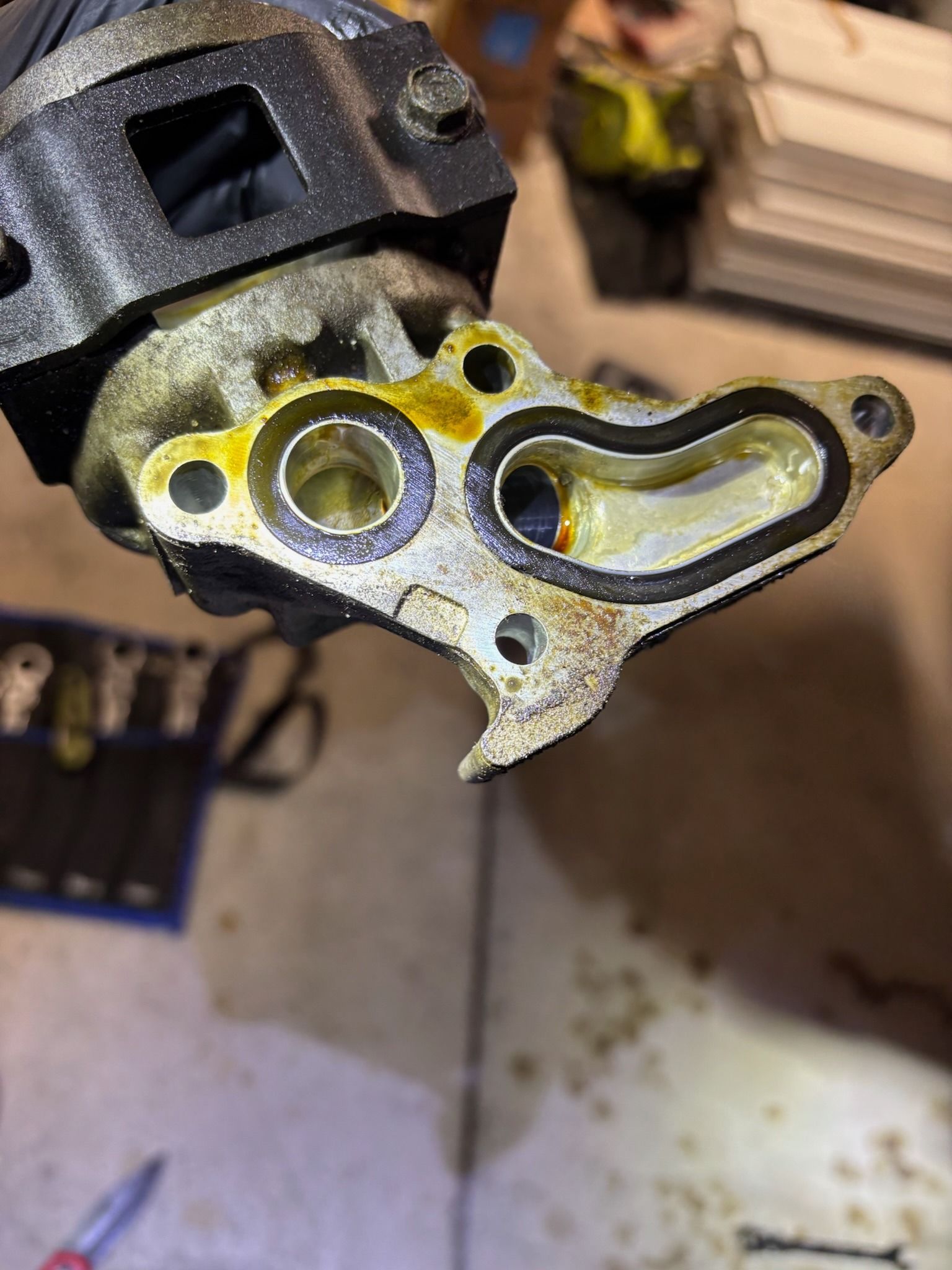 Close-up of a dirty metal engine gasket surface with bolt holes and oil residue.
