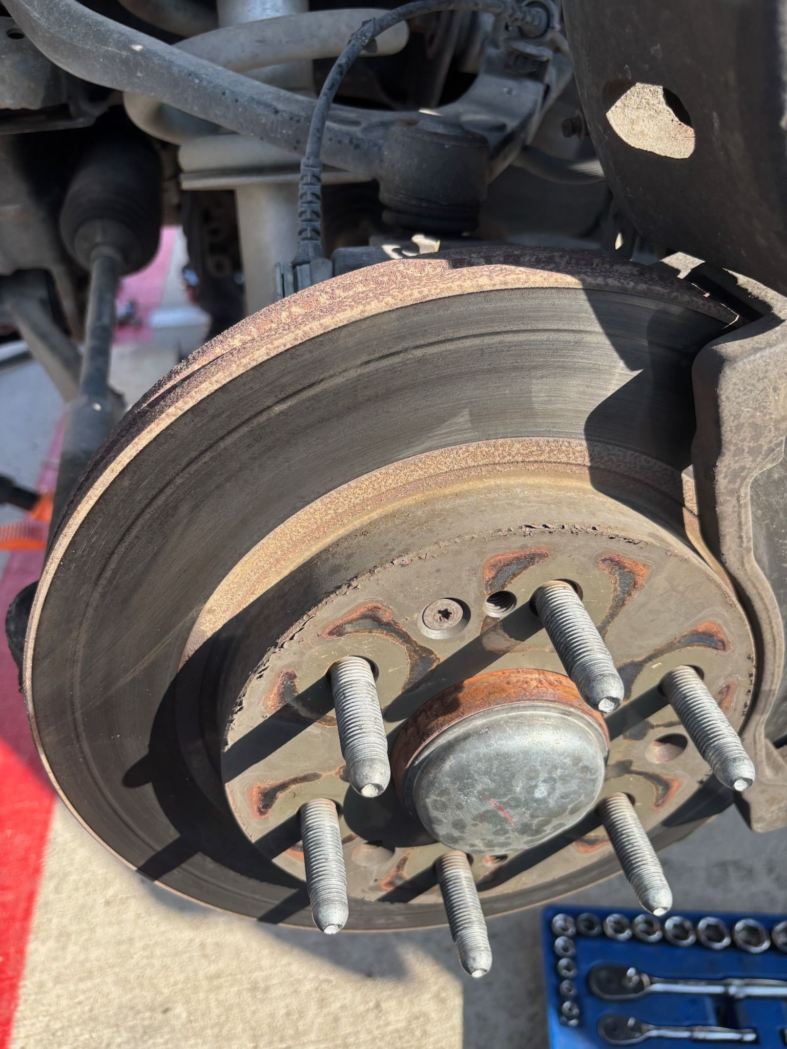 Close-up of a rusted car brake rotor and wheel hub with lug studs attached.