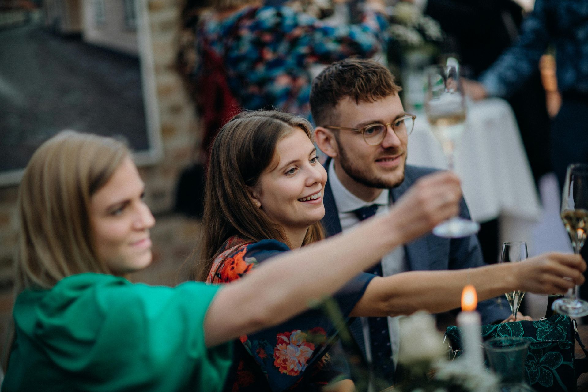 Drie mensen proosten met een drankje tijdens een avondbijeenkomst in de buitenlucht, glimlachend bi