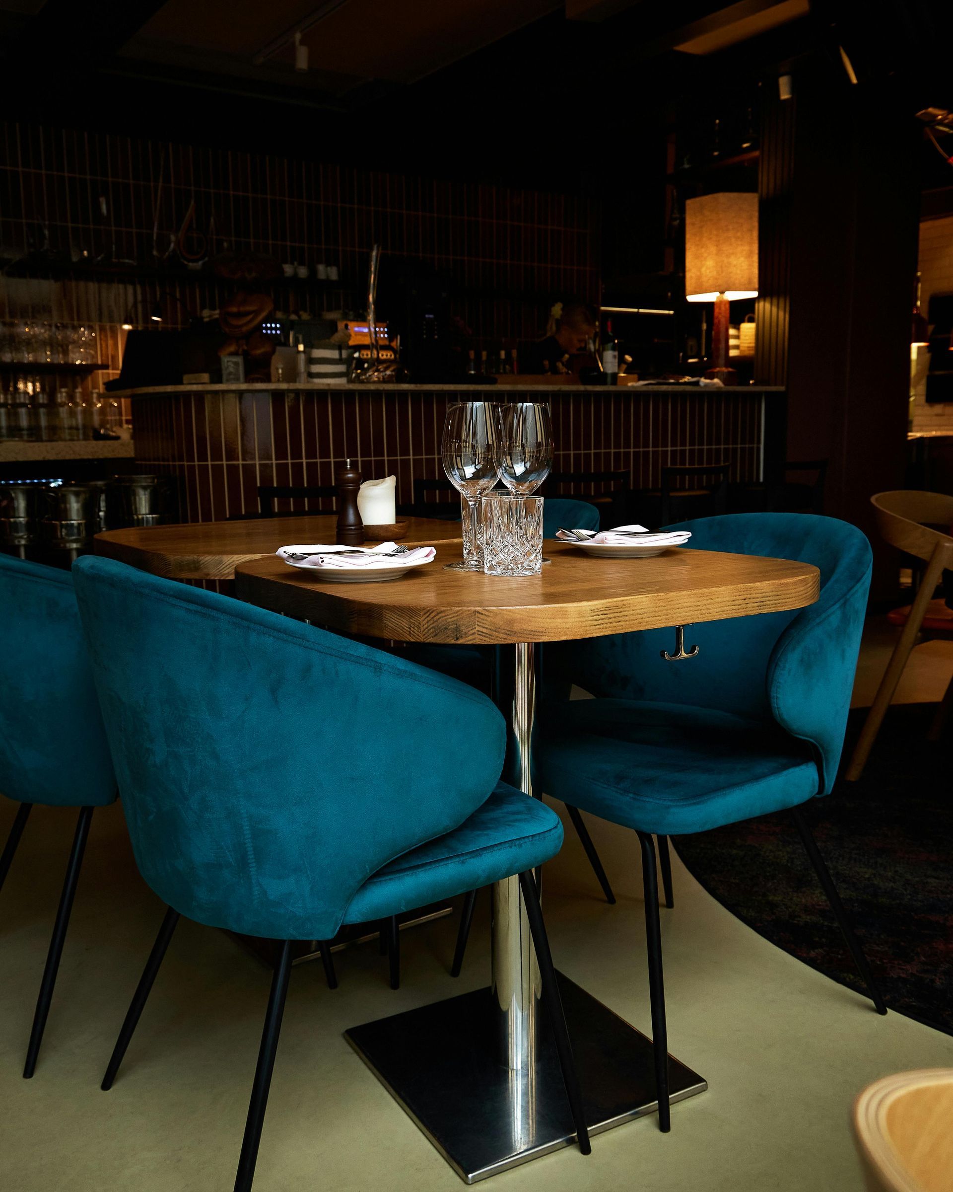 Turquoisekleurige stoelen rond een ronde tafel in een schemerig verlicht restaurantinterieur.