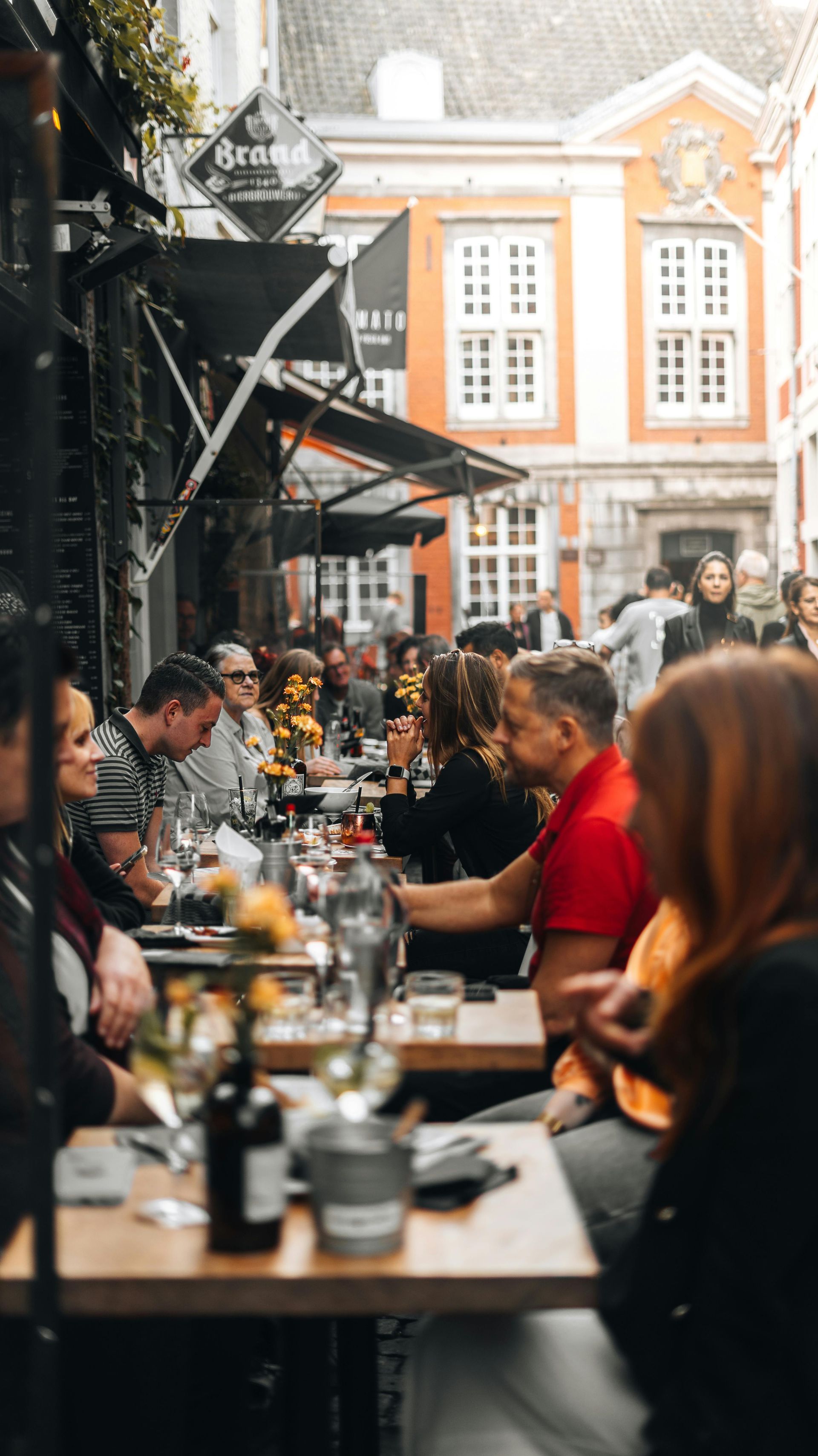 Een druk straatbeeld met terras en gasten aan tafel onder parasols zitten te eten