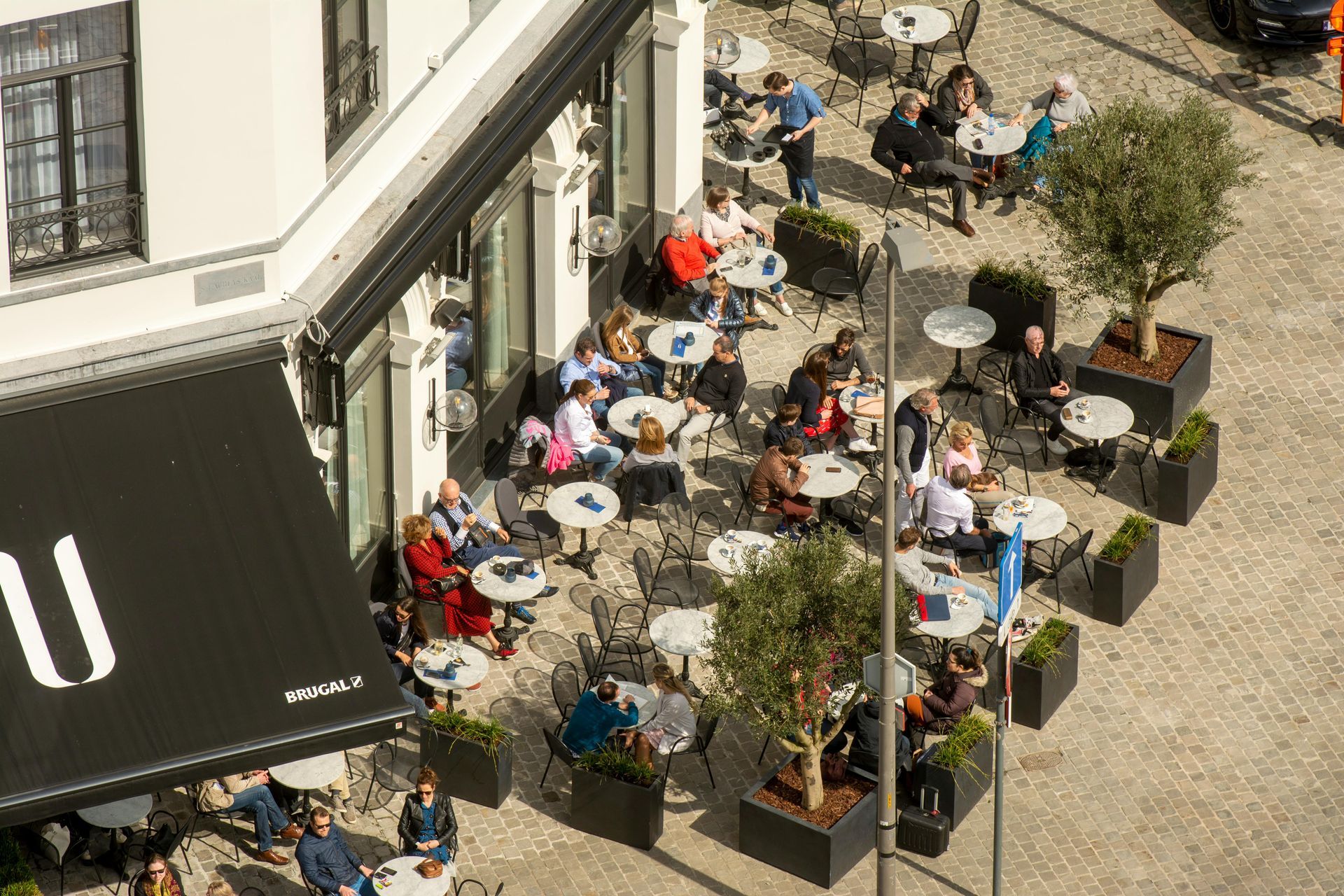 Terras van een café in de buitenlucht met veel mensen die aan tafels onder parasols naast een gebouw