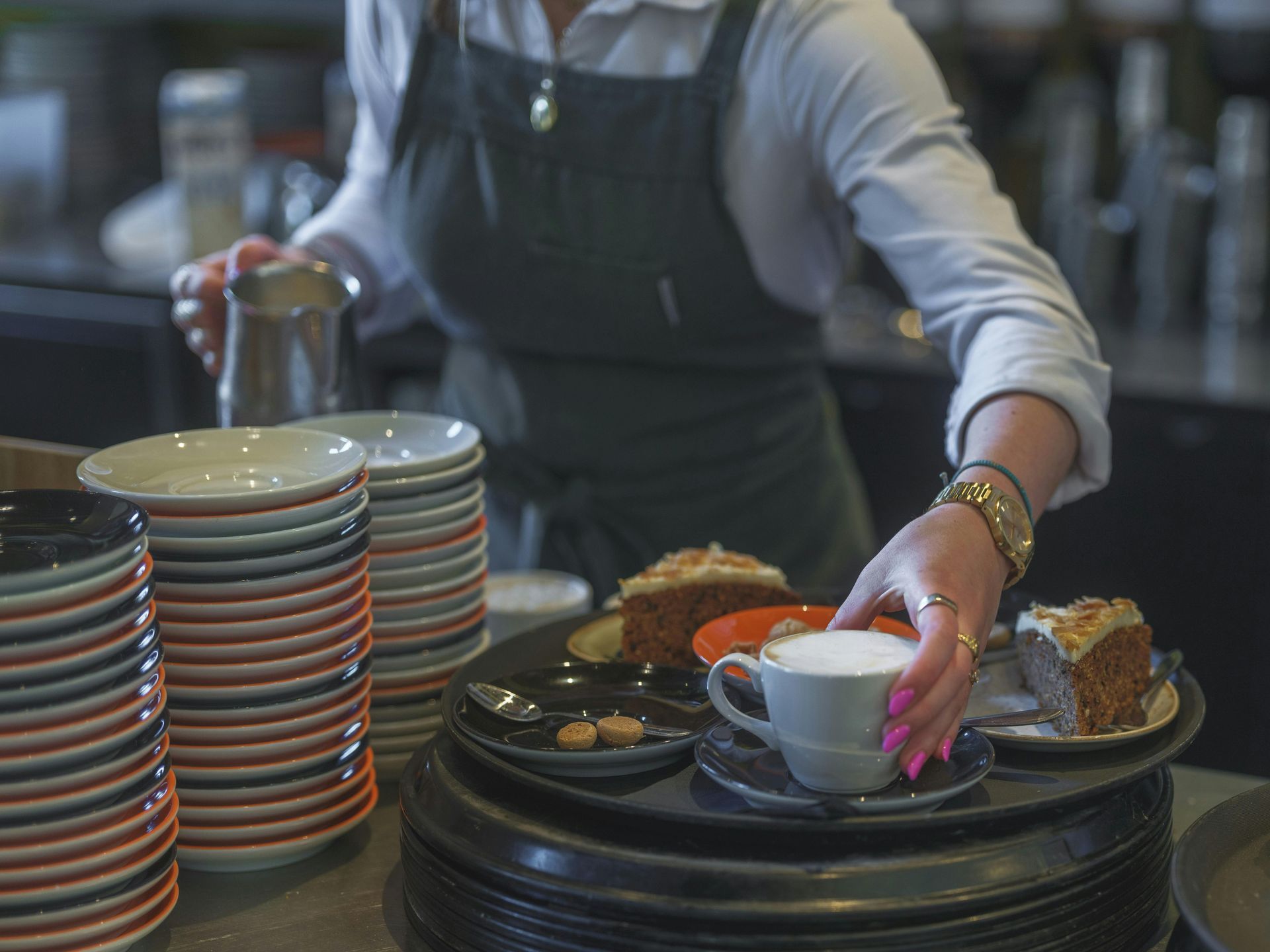 Een ober zet een kopje op een dienblad naast gestapelde borden in een restaurant