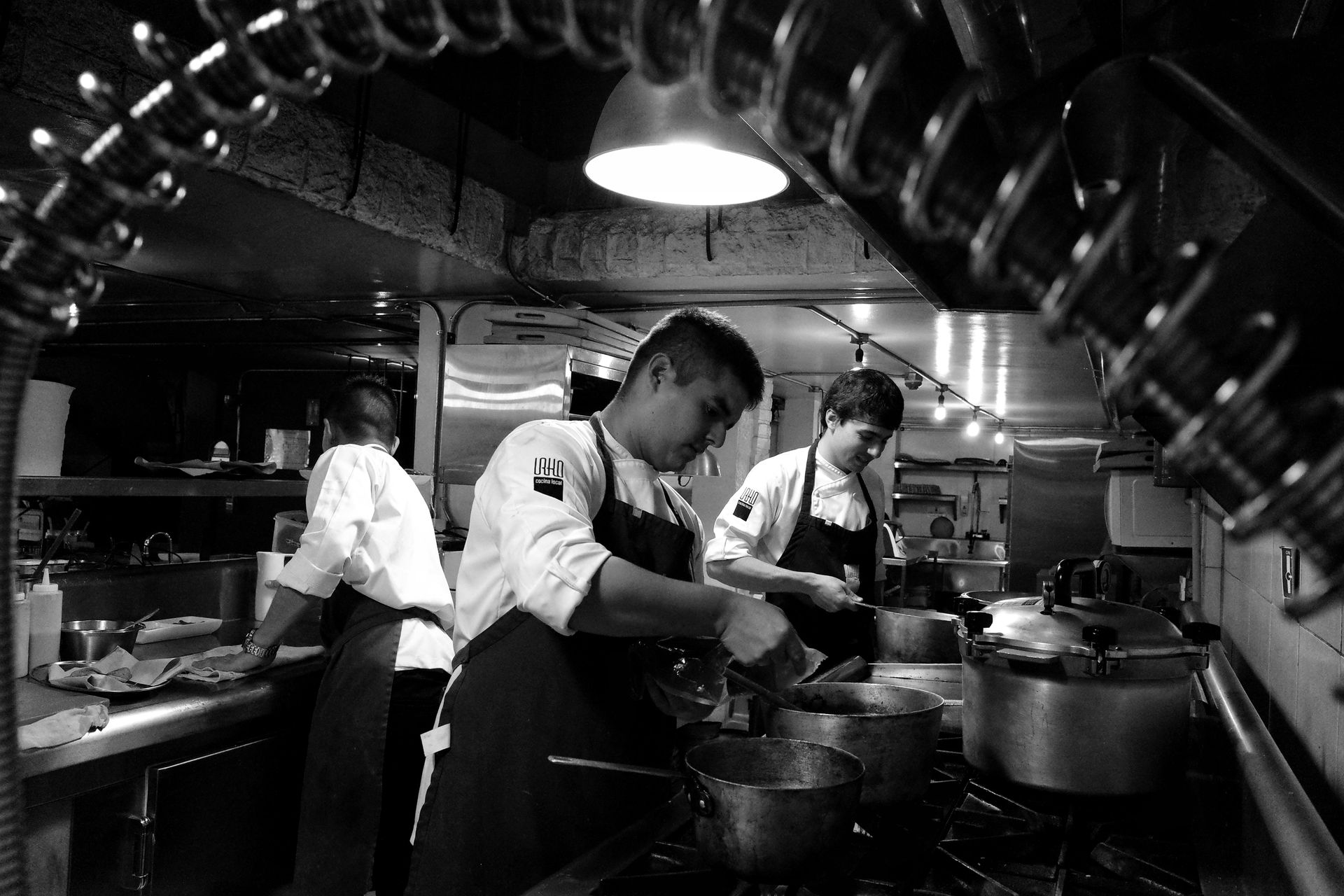 Koks werken in een drukke restaurantkeuken onder hangende lampen, roeren in pannen en bereiden eten