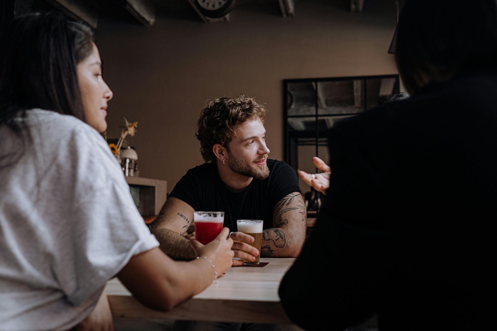 Drie mensen praten rond een tafel, één van hen houdt een rode mok vast