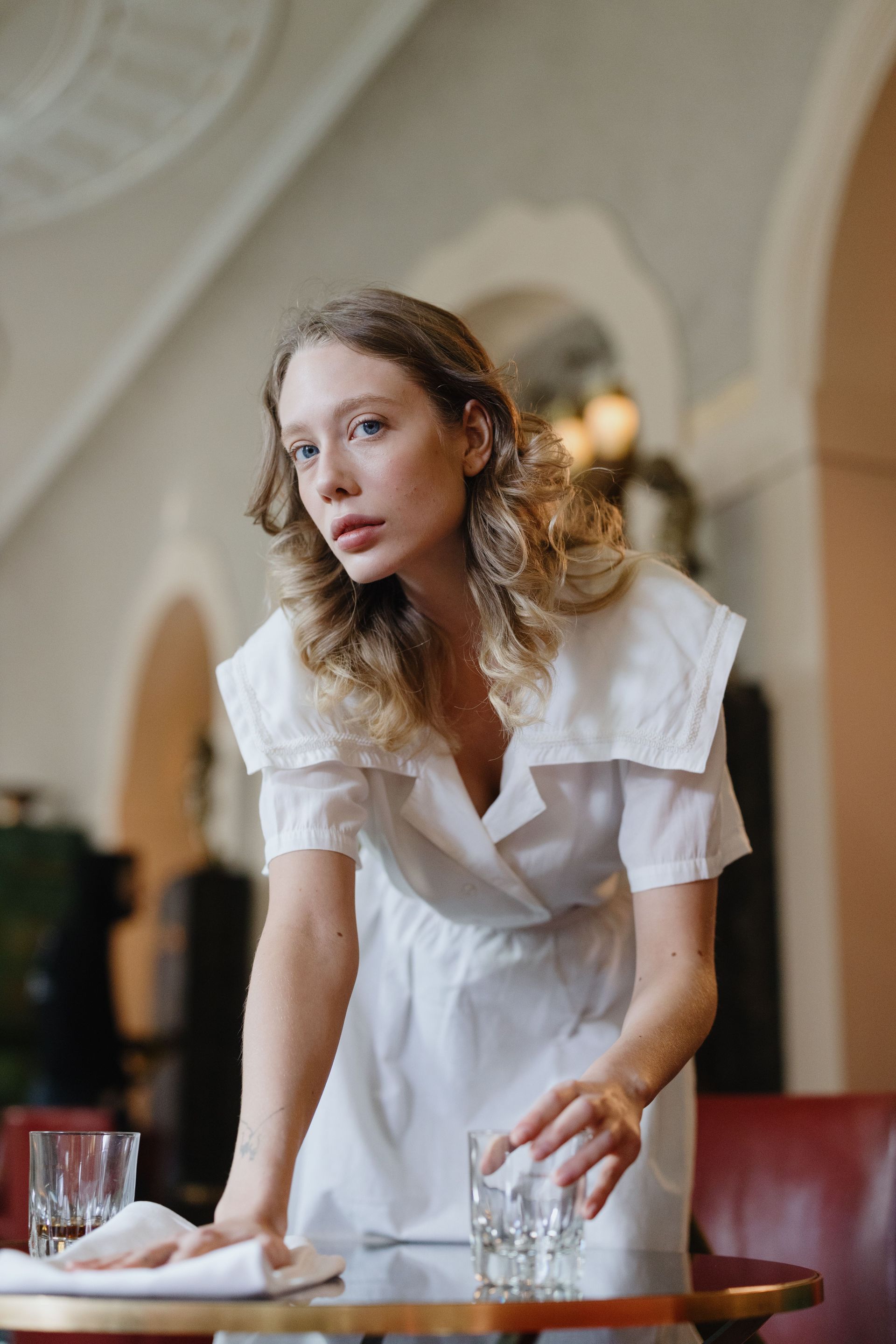 Vrouw in een witte jurk die over een tafel leunt in een sfeervol verlicht restaurant of café.