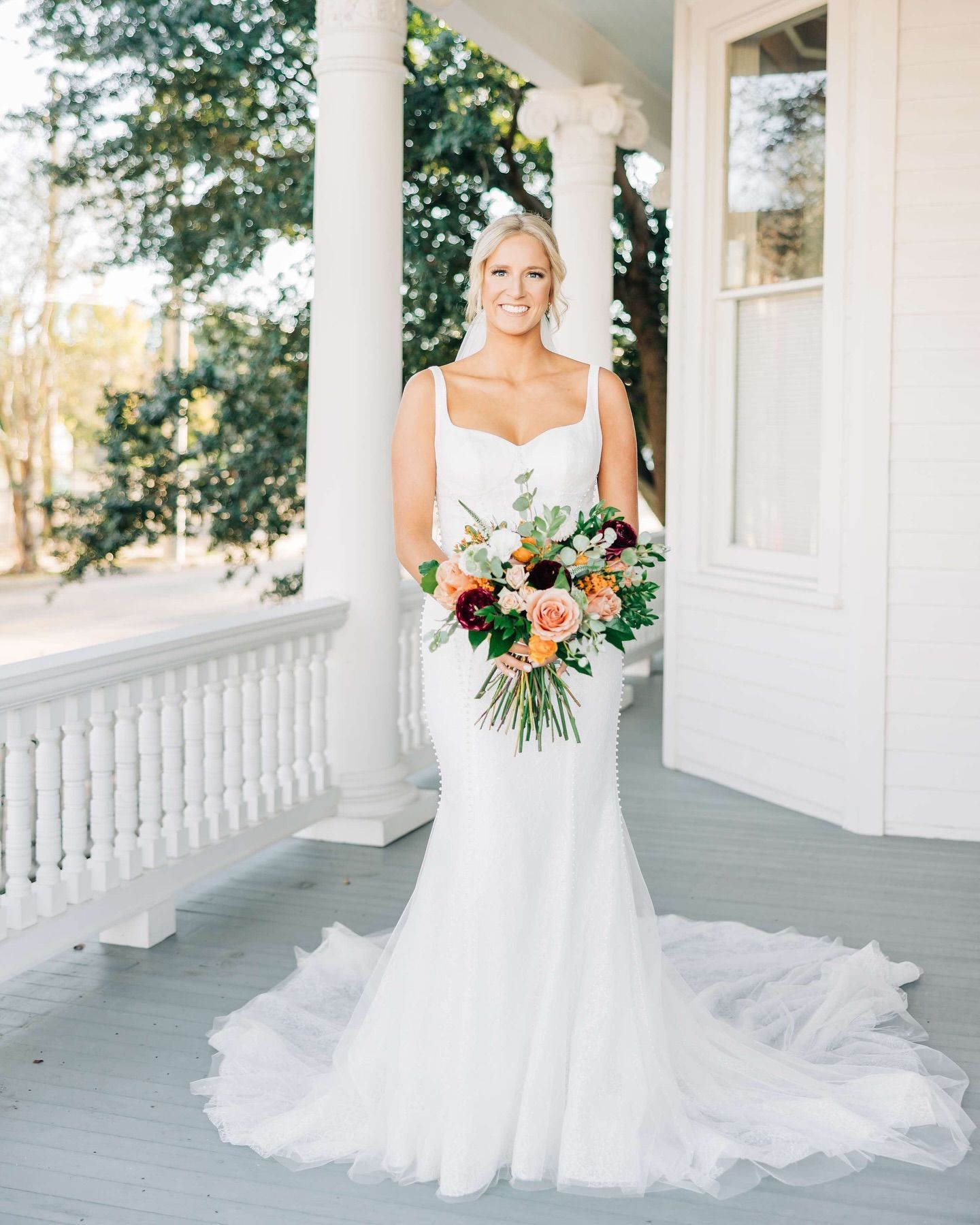 Bride in white dress holding bouquet on porch.