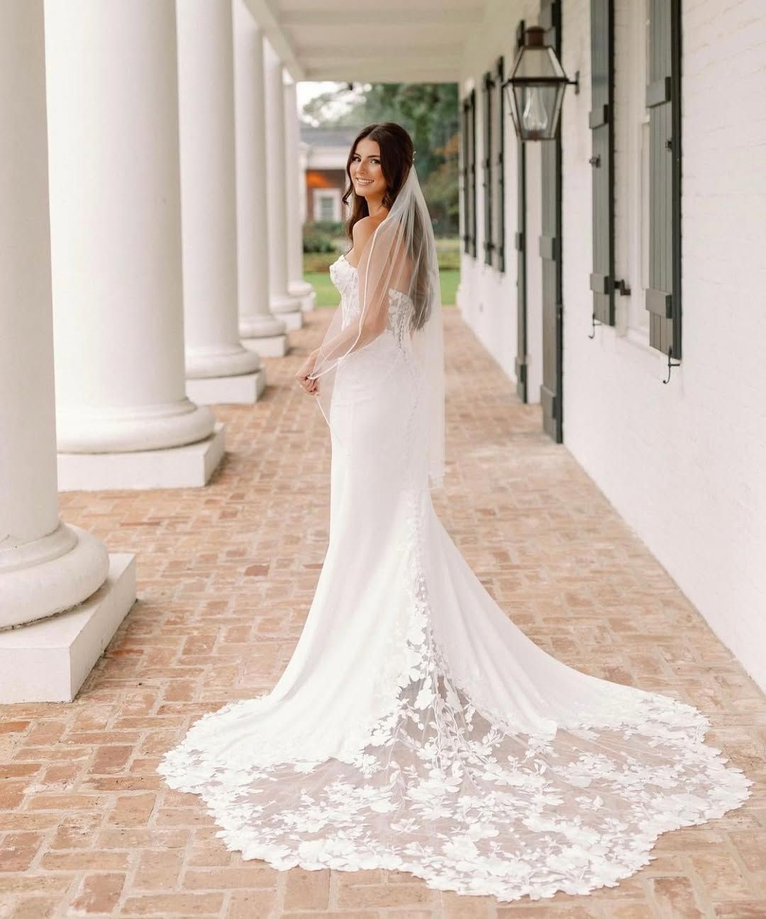 Bride in white gown with train, smiling, posing outside a white building with columns.
