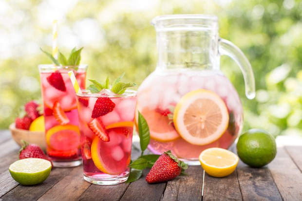 a pitcher and two glasses of strawberry lemonade on a wooden table .