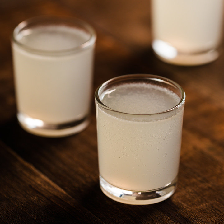 three shot glasses filled with white liquid on a wooden table