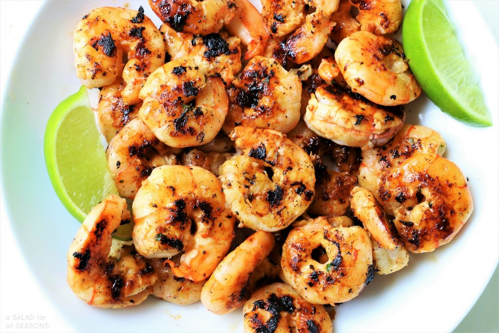 a white plate topped with shrimp and lime wedges .