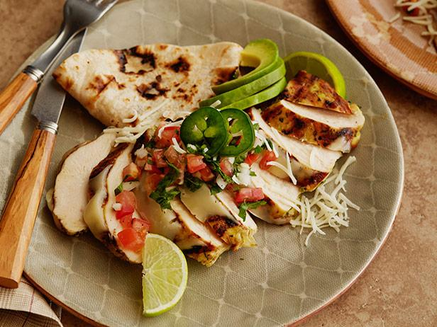 a plate of food with chicken , avocado , tomatoes and limes on a table .