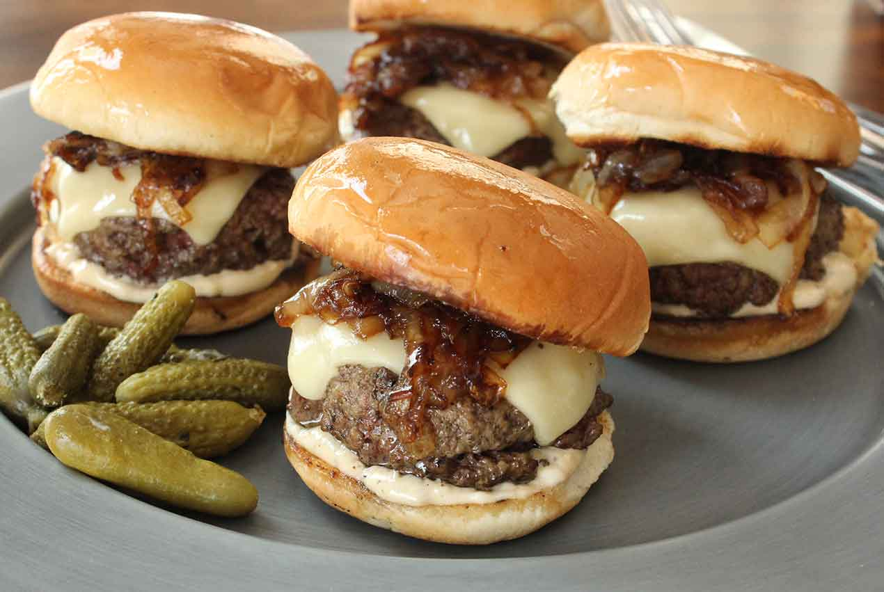 a plate of hamburgers and pickles on a table .