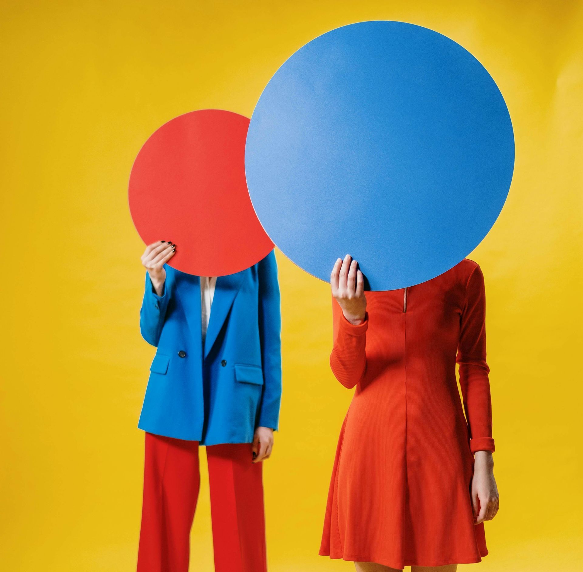 Two women are standing next to each other covering their faces with circles.