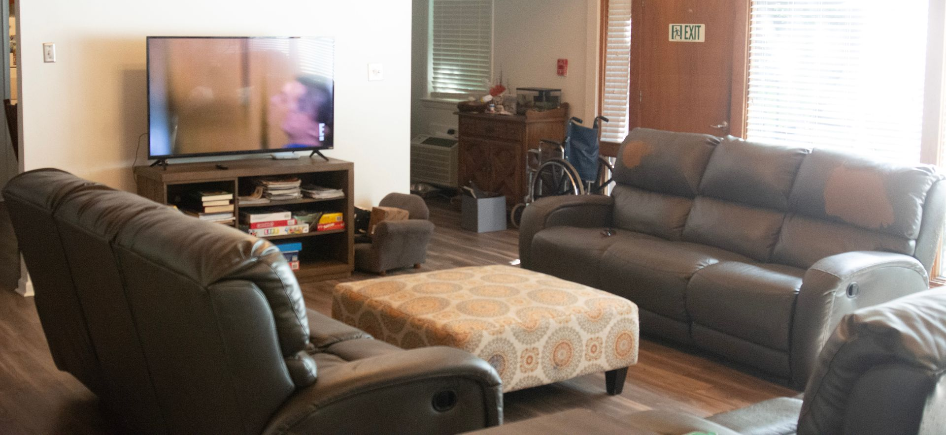 A bright living room with sofas, a TV, and an upholstered ottoman in an OGC residential home.