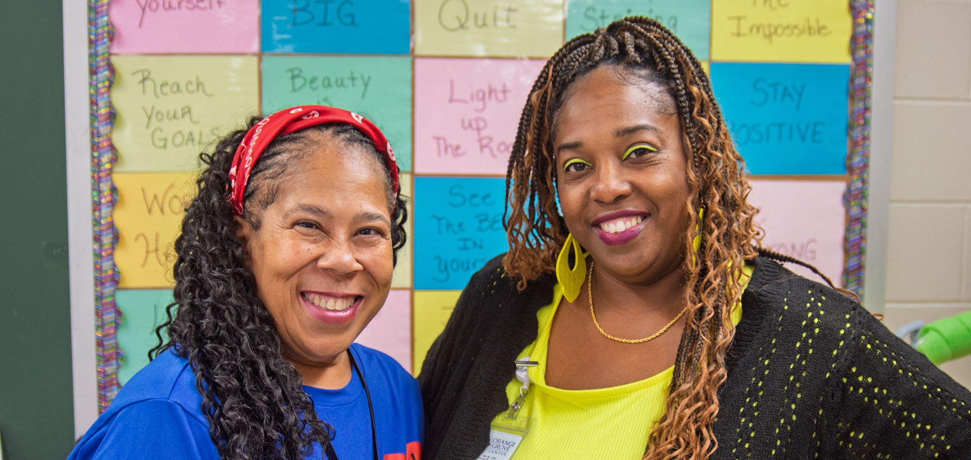 Two female Direct Support Professionals smiling while standing in one of Orange Grove's classrooms.