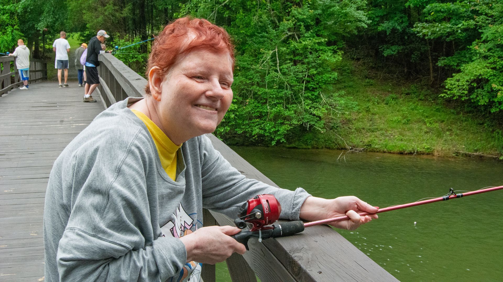 A female camper holds her fishing rod and smiles at the camera.
