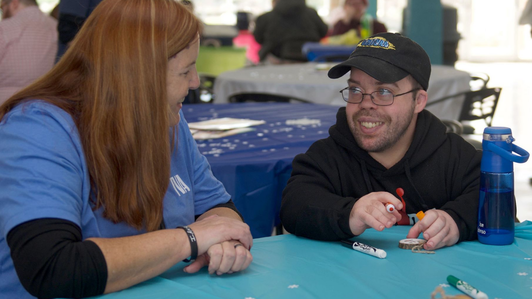A man supported by Orange Grove smiles a female TVA volunteer sitting next to him in Orange Grove's cafeteria.