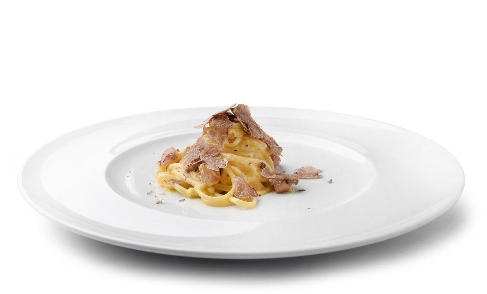 Un piatto bianco con sopra spaghetti e carne su uno sfondo bianco.