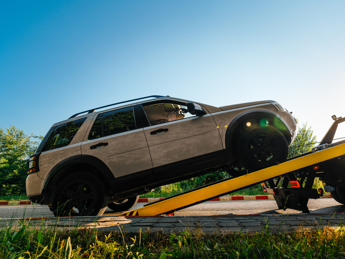 SUV being loaded onto a tow truck ramp in bright sunlight