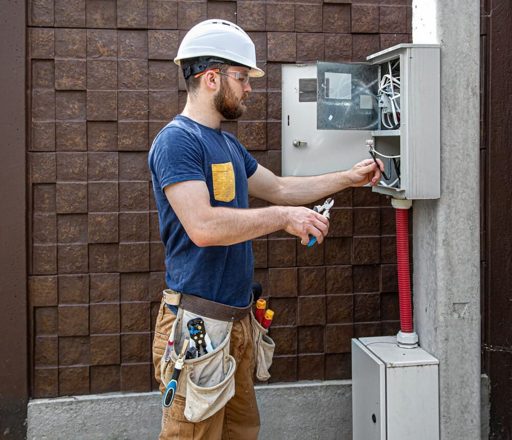 Man Wearing a Hard Hat and Safety Glasses is Working on an Electrical Box — J.A.F. Electrical Solutions in Gracemere, QLD