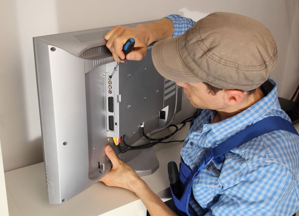 A Man is Fixing a Flat Screen Tv With a Screwdriver — J.A.F. Electrical Solutions in Gracemere, QLD