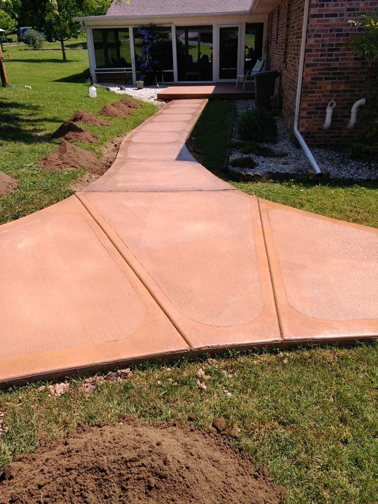 Concrete walkway leading to a house with glass doors, set in a grassy yard.