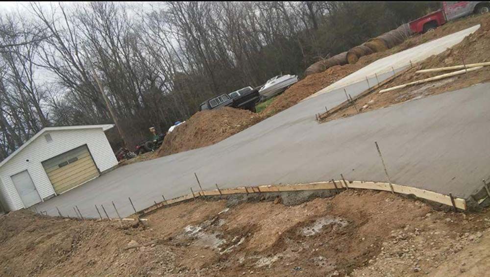 A newly poured concrete driveway winds toward a white garage on a cloudy day; construction site.